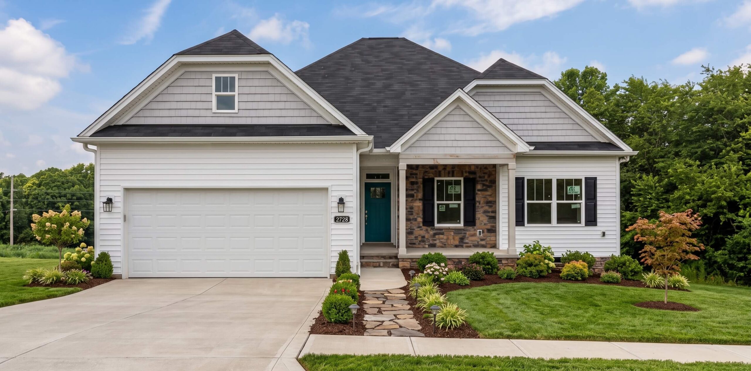 Front elevation of a new single-story white and stone craftsman-style home with a dark gray shingled roof, a paved driveway leading to a two-car garage, and freshly landscaped green lawn with flower beds and a stone walkway.